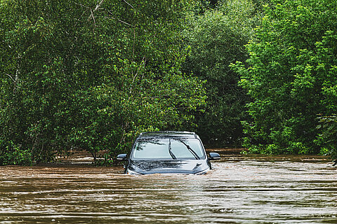 Ein Auto steht bis zu den Fensterscheiben in Wasser. Im Hintergund stehen Bäume.