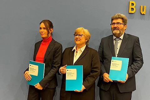 Das Foto zeigt die Oberkörper dreier stehender Personen des Deutschen Instituts für Menschenrechte vor der blauen Wand eines Veranstaltungsraumes im Haus der Bundespressekonferenz. Sie halten jeweils eine Druckausgabe des Menschenrechtssituationsbericht 2024 in den Händen und lächeln. Von links nach rechts sind abgebildet: Nele Allenberg, Leitung der Abteilung Menschenrechtspolitik Inland/Europa, Beate Rudolf, Direktorin des Instituts, und Michael Windfuhr, Stellvertretender Direktor des Instituts.